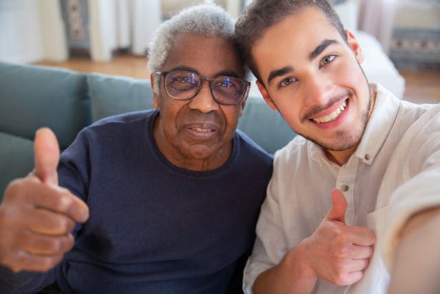 Male assisted living staff giving two thumbs up, endorsing the quality service provided under affordable long-term care insurance plans for pre-retirees.